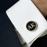 Cufflinks with 'AK' initials on a white shirt cuff against a dark background