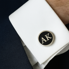 Cufflinks with 'AK' initials on a white shirt cuff against a dark background